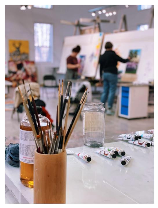 Artists painting in studio in background cup of paintbrushes in foreground
