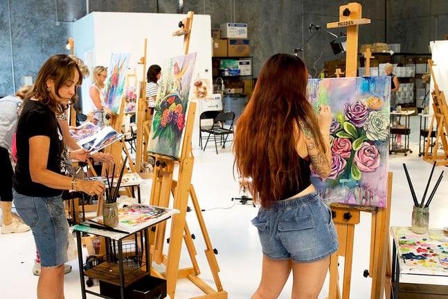 Artists painting flowers in group on easels 