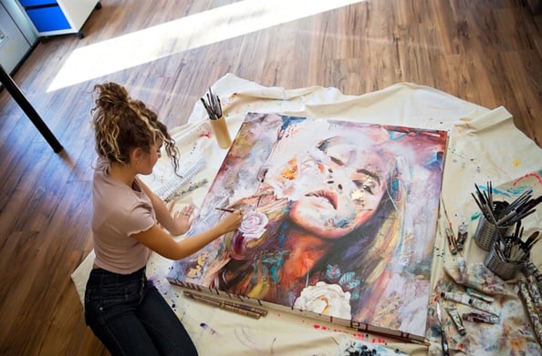 girl painting a portrait on the ground over a canvas