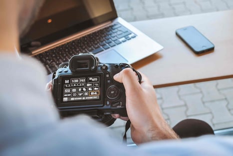 hand holding camera with desk with laptop
