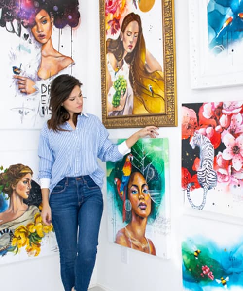 woman in blue standing in gallery with colorful portrait paintings 