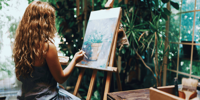 woman sitting at easel with palnt art 