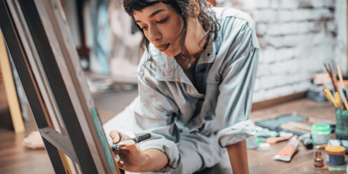 Girls in blue grey shirt stitting in front of art canvas drawing