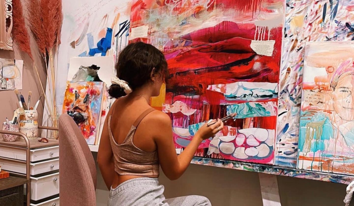 woman sitting in front of red white painting painting with paintbrush